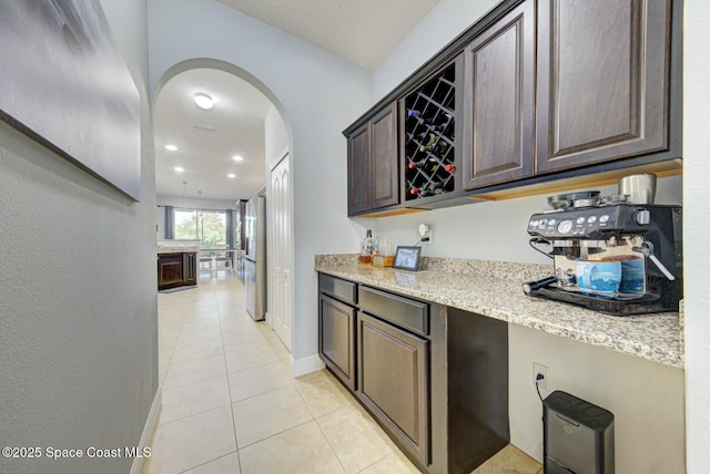 kitchen featuring dark brown cabinetry, light stone counters, stainless steel fridge, and light tile patterned flooring