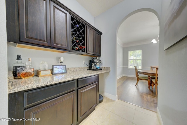 bar featuring ornamental molding, dark brown cabinets, light stone countertops, and light tile patterned flooring