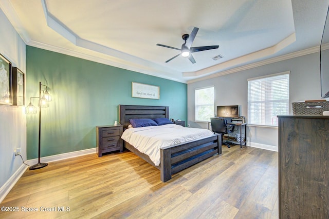 bedroom with light wood finished floors, a tray ceiling, ornamental molding, and baseboards