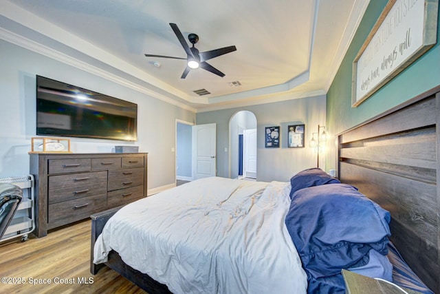 bedroom featuring arched walkways, crown molding, a raised ceiling, visible vents, and light wood-style floors