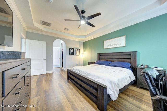 bedroom featuring visible vents, arched walkways, ornamental molding, a tray ceiling, and light wood-style floors