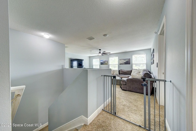 hall featuring baseboards, visible vents, an upstairs landing, a textured ceiling, and carpet flooring