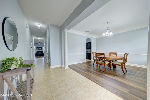 dining room featuring a notable chandelier, light tile patterned floors, baseboards, ornamental molding, and ornate columns