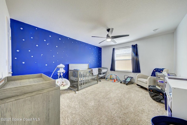 unfurnished bedroom with carpet floors, ceiling fan, a crib, and a textured ceiling