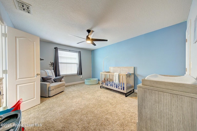 bedroom with a textured ceiling, light colored carpet, a ceiling fan, visible vents, and a crib