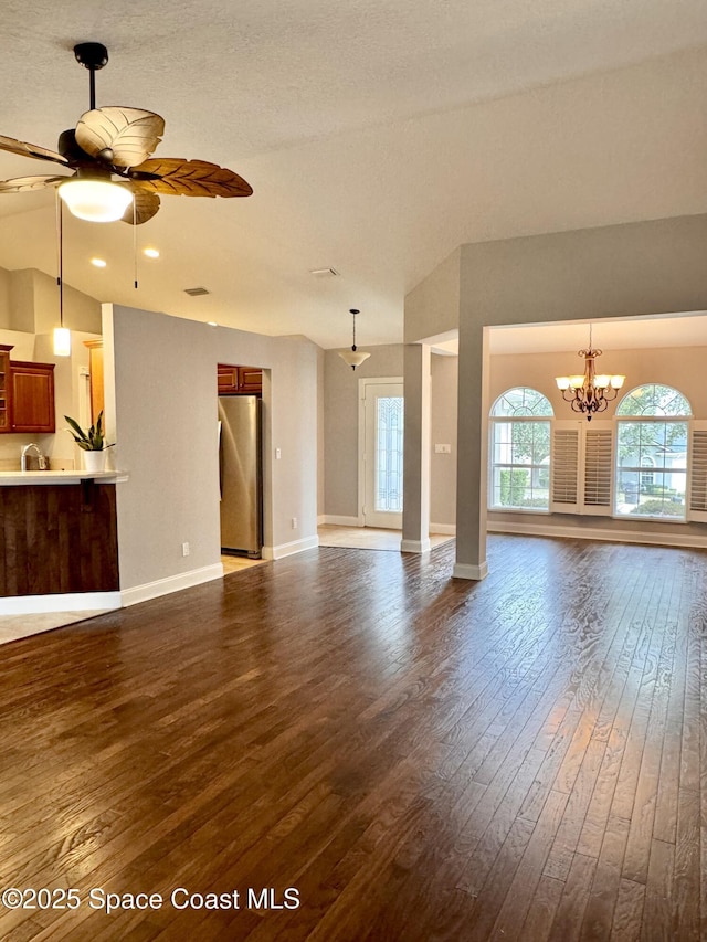 unfurnished living room with vaulted ceiling, ceiling fan with notable chandelier, a textured ceiling, and dark hardwood / wood-style flooring