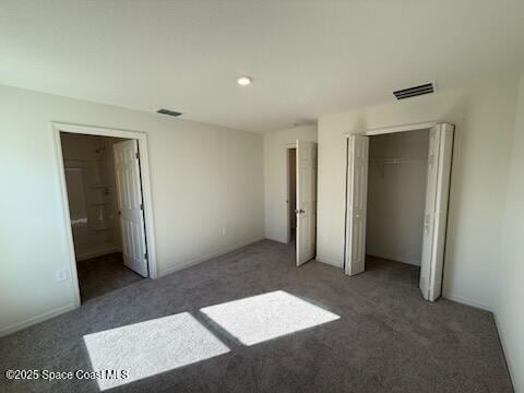 unfurnished bedroom featuring dark colored carpet, ensuite bath, and a closet