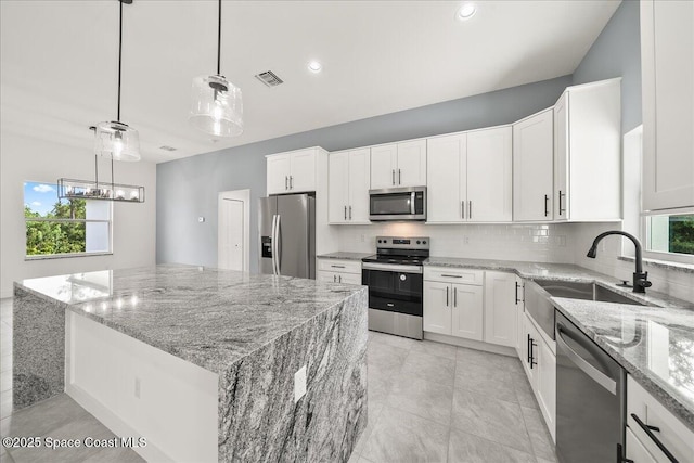 kitchen with a center island, appliances with stainless steel finishes, white cabinetry, sink, and decorative light fixtures