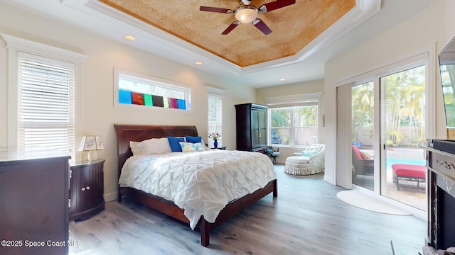 bedroom featuring wood-type flooring, access to exterior, crown molding, and a tray ceiling