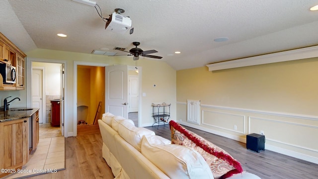 living room featuring lofted ceiling, sink, a textured ceiling, and light wood-type flooring