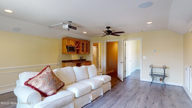 living room with vaulted ceiling, sink, ceiling fan, light hardwood / wood-style floors, and a textured ceiling