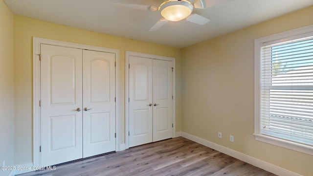 unfurnished bedroom featuring ceiling fan, two closets, and light wood-type flooring