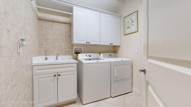 clothes washing area with light tile patterned flooring, sink, cabinets, washer and dryer, and tile walls