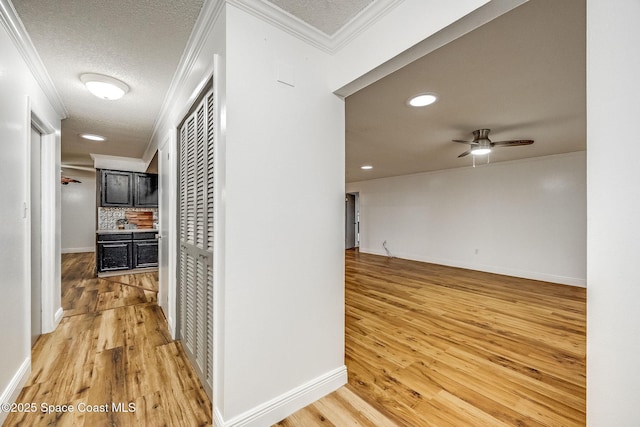 hallway with ornamental molding, a textured ceiling, and light hardwood / wood-style floors