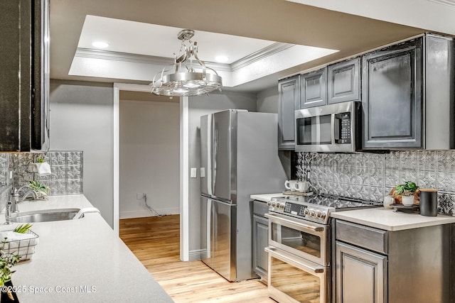 kitchen with sink, hanging light fixtures, ornamental molding, appliances with stainless steel finishes, and a tray ceiling