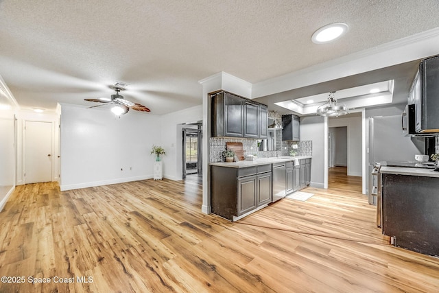 kitchen featuring crown molding, light hardwood / wood-style flooring, appliances with stainless steel finishes, tasteful backsplash, and a raised ceiling