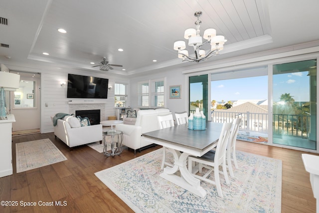 dining area with hardwood / wood-style floors, a tray ceiling, and ceiling fan with notable chandelier