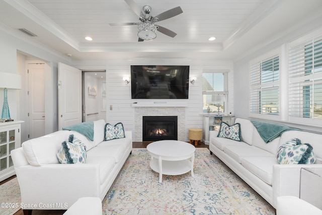 living room with a tray ceiling, ornamental molding, ceiling fan, and light wood-type flooring