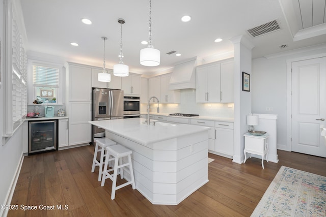 kitchen featuring custom exhaust hood, appliances with stainless steel finishes, a kitchen island with sink, and white cabinets