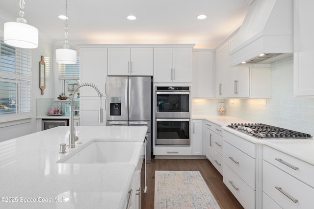 kitchen featuring stainless steel appliances, premium range hood, pendant lighting, and white cabinets