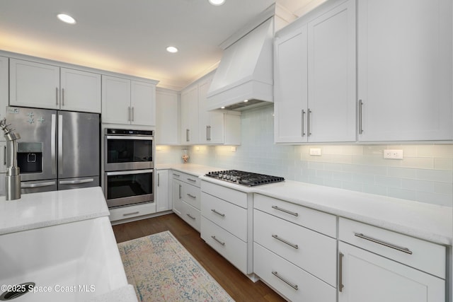 kitchen featuring tasteful backsplash, stainless steel appliances, custom range hood, and white cabinets