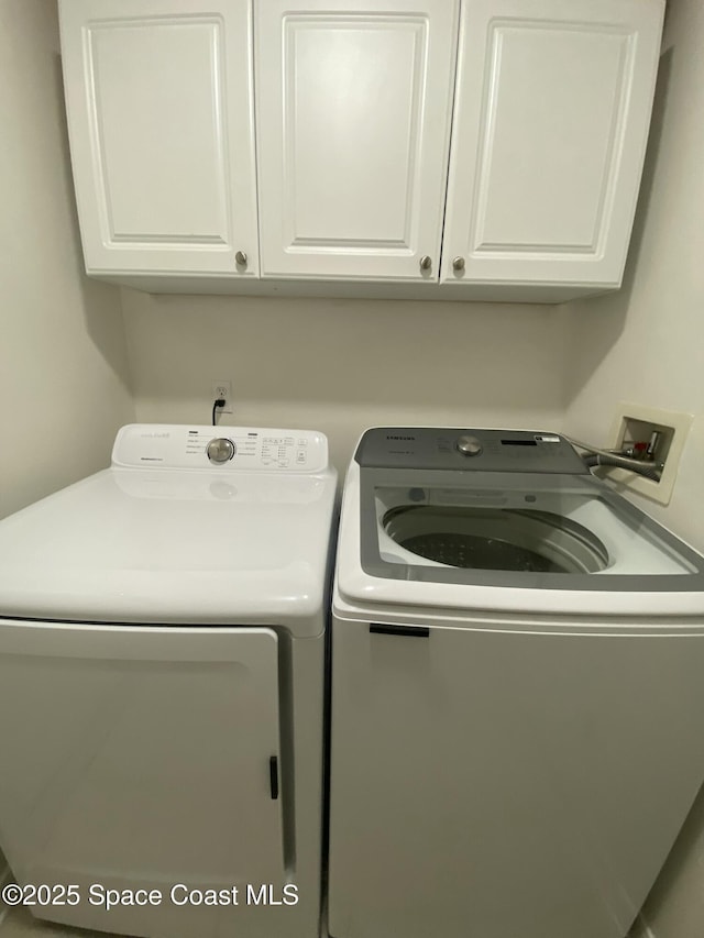 clothes washing area with cabinets and washing machine and clothes dryer