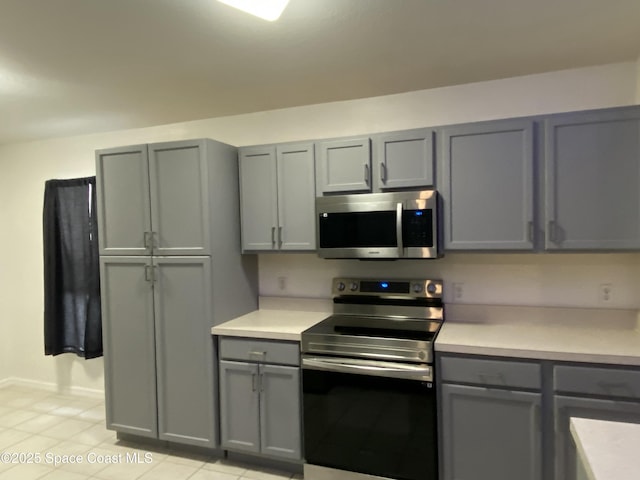 kitchen with stainless steel appliances, light tile patterned floors, and gray cabinetry