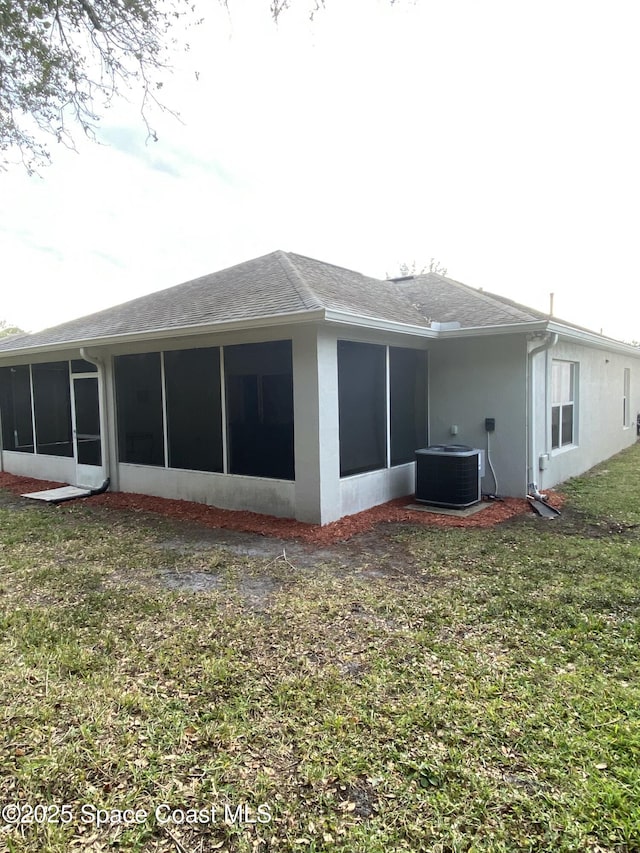 rear view of house with central AC unit, a lawn, and a sunroom