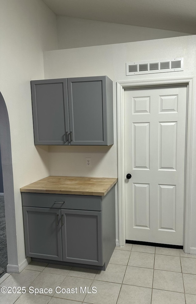 kitchen featuring gray cabinets, vaulted ceiling, light tile patterned floors, and wooden counters