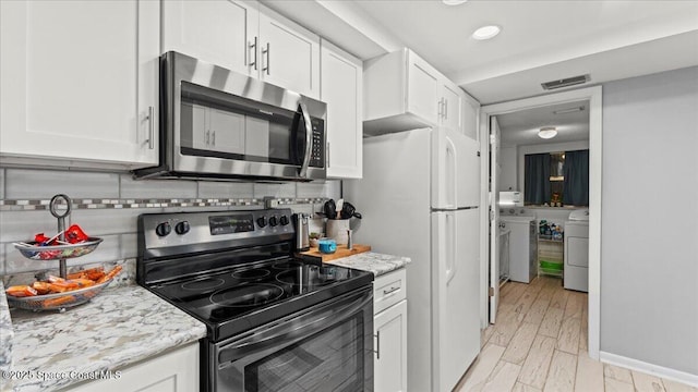 kitchen with white cabinetry, stainless steel appliances, washing machine and dryer, tasteful backsplash, and light stone countertops