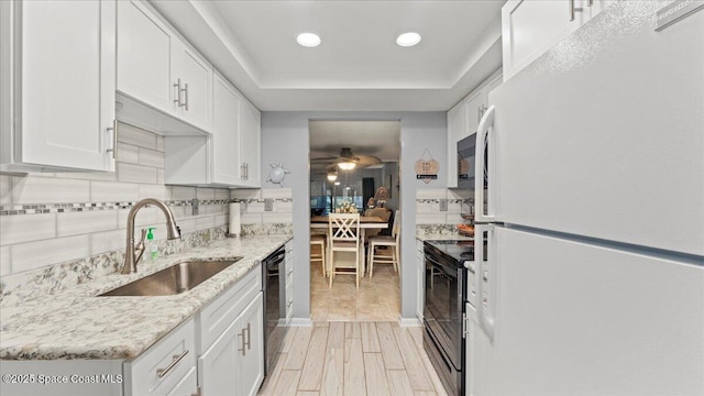 kitchen featuring sink, white cabinetry, backsplash, black appliances, and light stone countertops