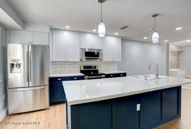 kitchen featuring appliances with stainless steel finishes, decorative light fixtures, white cabinetry, sink, and a kitchen island with sink