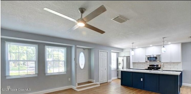 kitchen with stainless steel appliances, hanging light fixtures, a center island with sink, and white cabinets