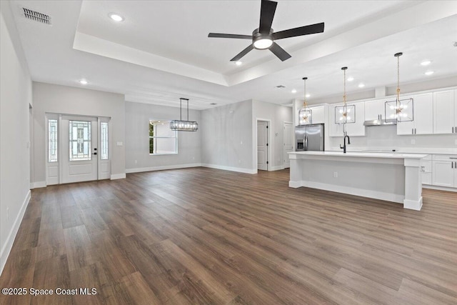 unfurnished living room with sink, ceiling fan with notable chandelier, dark hardwood / wood-style flooring, and a tray ceiling