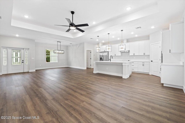 unfurnished living room with dark hardwood / wood-style flooring, ceiling fan with notable chandelier, and a raised ceiling