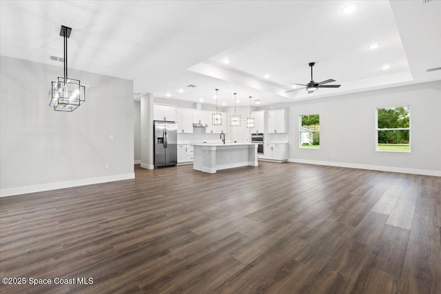 unfurnished living room featuring sink, ceiling fan with notable chandelier, dark hardwood / wood-style floors, and a tray ceiling