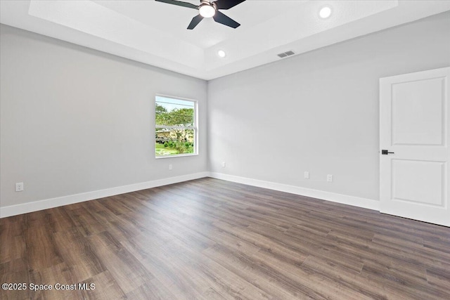 unfurnished room with ceiling fan, a tray ceiling, and dark hardwood / wood-style flooring