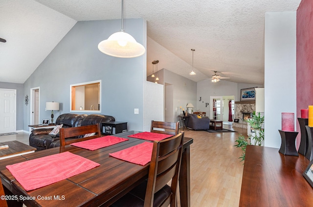 dining space featuring ceiling fan, a stone fireplace, vaulted ceiling, and light hardwood / wood-style flooring