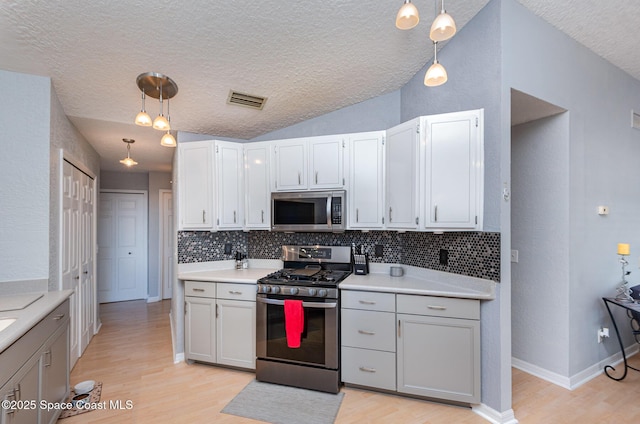 kitchen featuring stainless steel appliances, decorative light fixtures, vaulted ceiling, and light hardwood / wood-style flooring