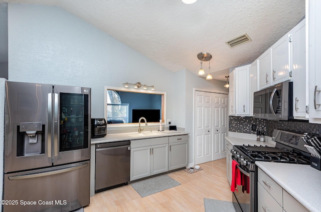 kitchen featuring appliances with stainless steel finishes, white cabinetry, lofted ceiling, sink, and hanging light fixtures