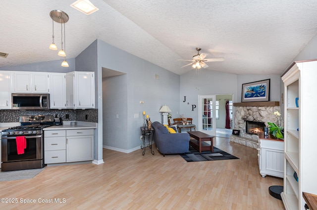 kitchen featuring white cabinetry, decorative light fixtures, vaulted ceiling, stainless steel appliances, and light hardwood / wood-style floors