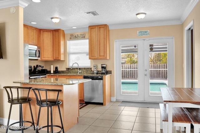 kitchen featuring sink, a breakfast bar area, appliances with stainless steel finishes, light stone countertops, and french doors