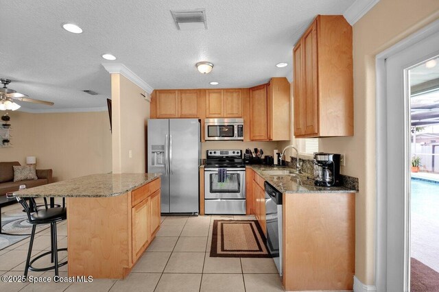 kitchen with sink, light stone counters, ornamental molding, appliances with stainless steel finishes, and a kitchen island