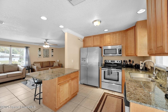 kitchen featuring sink, a kitchen island, light stone countertops, and appliances with stainless steel finishes