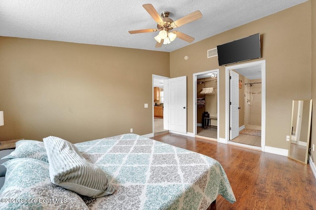 bedroom featuring a walk in closet, wood-type flooring, vaulted ceiling, and a textured ceiling