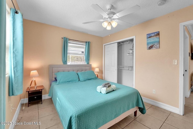 bedroom featuring ceiling fan, light tile patterned floors, a closet, and a textured ceiling