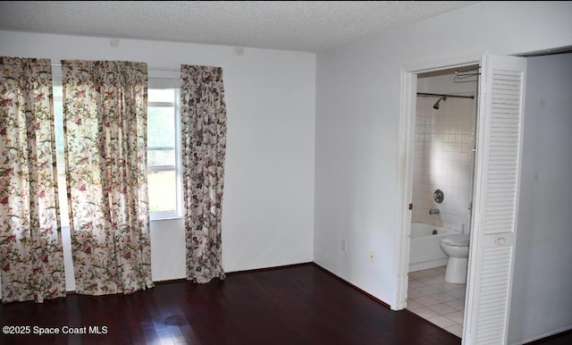 unfurnished bedroom featuring multiple windows, ensuite bath, a textured ceiling, and hardwood / wood-style flooring