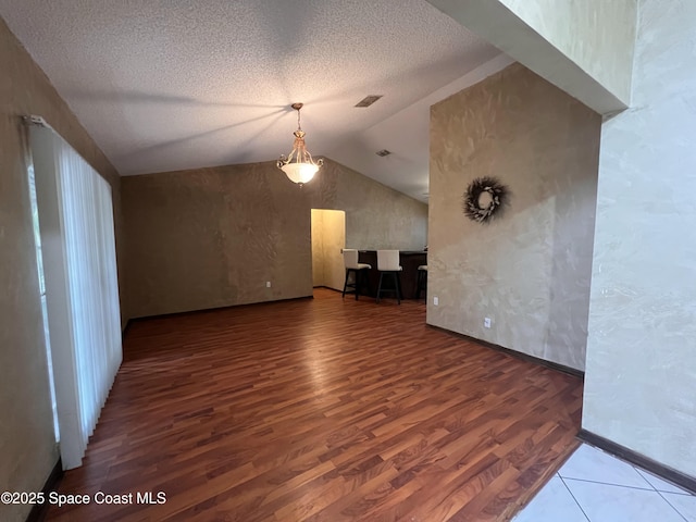 unfurnished living room with vaulted ceiling, a textured ceiling, and wood-type flooring