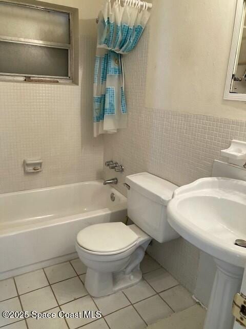 bathroom with tile patterned flooring, tiled shower / bath combo, tile walls, and toilet