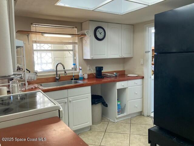 kitchen featuring black refrigerator, sink, white cabinets, and light tile patterned floors